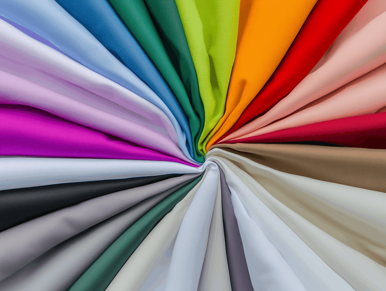 Eine radiale Anordnung von bunten Stoffmustern, die kreisförmig aufgefächert sind und in der Mitte zusammenlaufen und eine breite Palette von leuchtenden und gedämpften Farbtönen wie Rot, Grün, Blau, Gelb, Lila, Braun und Grau zeigen.