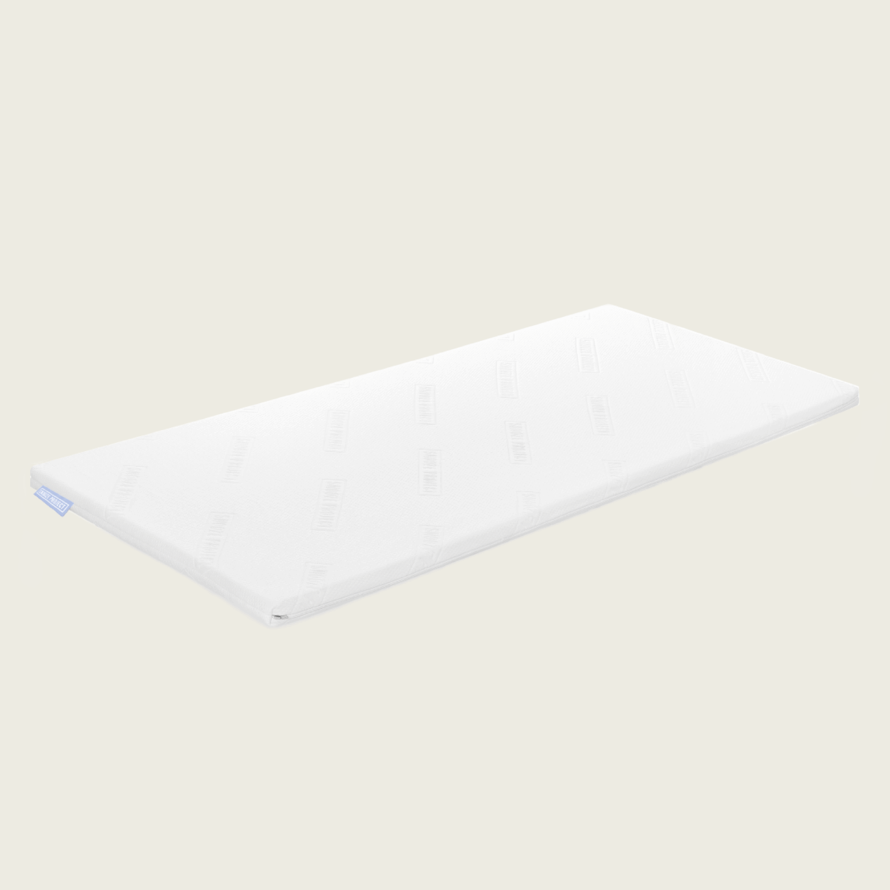 topper-allgemein-3 Ein schmaler, rechteckiger Familienbett Topper in Weiß mit leicht abgerundeten Ecken ruht auf einem unifarbenen, hellen Hintergrund und ist mit einem dezenten Muster und einem kleinen Stoffanhänger an einer Kante versehen.
