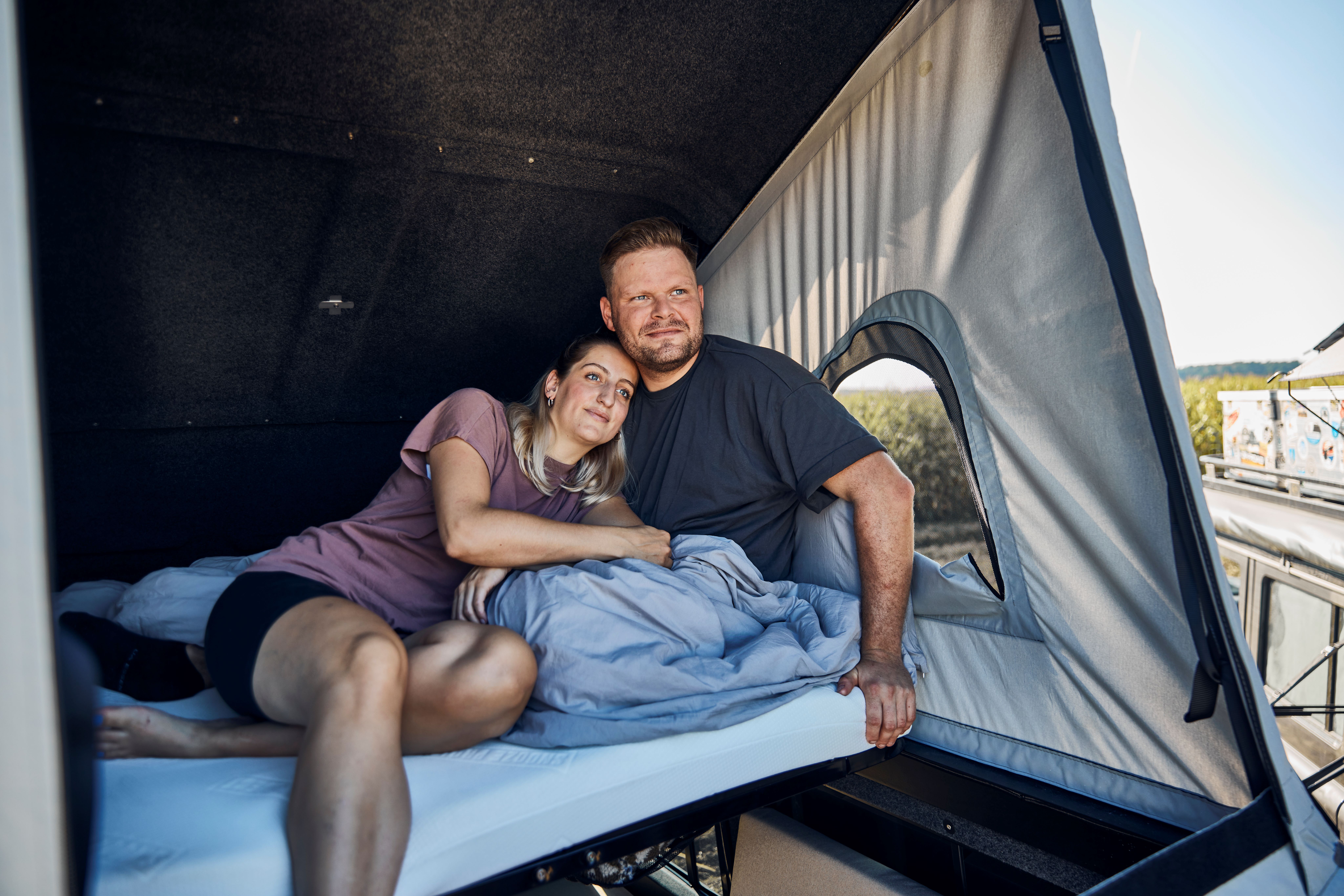 Nils und Kira lehnen in ihrem Bett im Hubdach des Defenders aneinander.