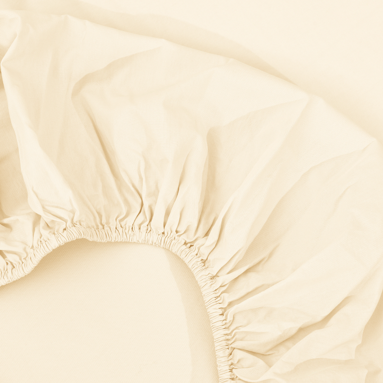 spannbettlaken nach maß creme 2 Nahaufnahme eines beigen Spannbettlakens mit gerafften Gummirändern, ausgebreitet auf einer passenden hellen Unterlage.