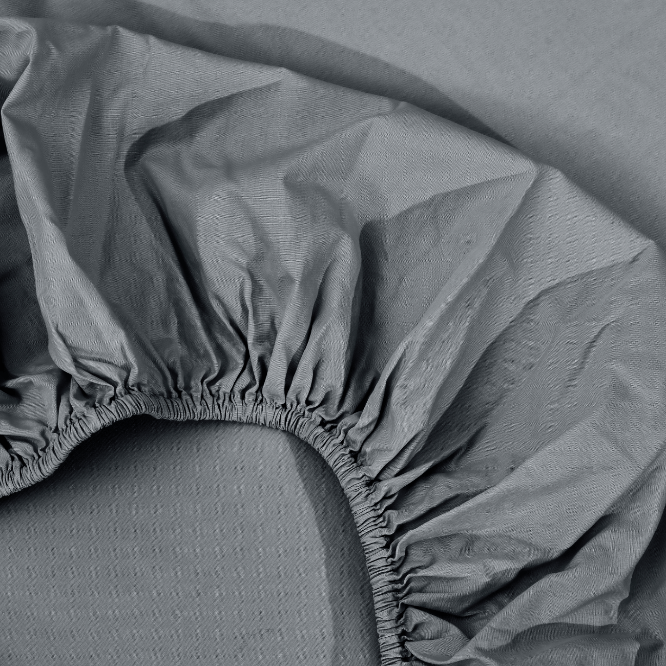 spannbettlaken nach maß grau 2 Nahaufnahme eines grauen Spannbettlakens mit gerafften Gummirändern, ausgebreitet auf einer passenden grauen Fläche.