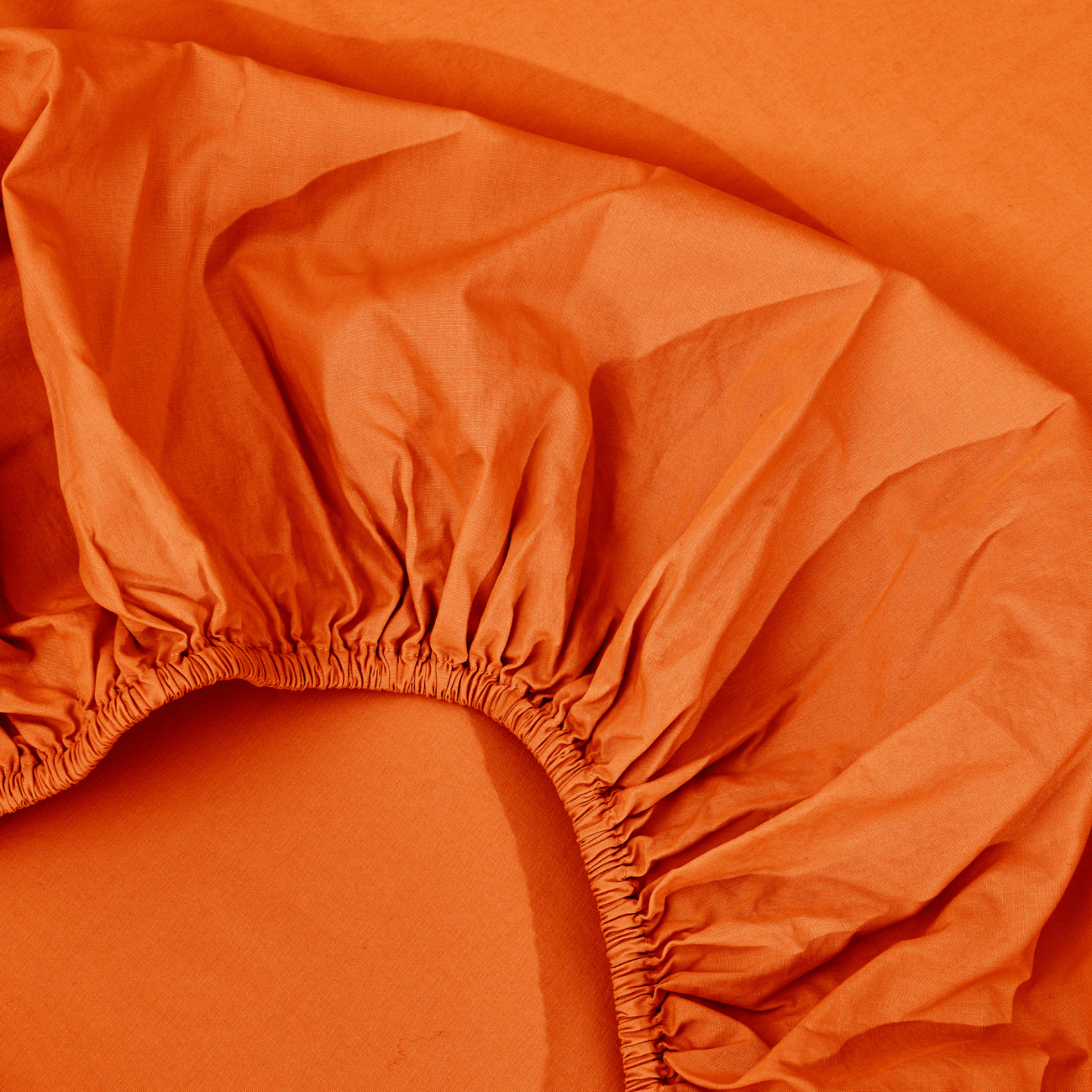 spannbettlaken nach maß orange 2 Eine Nahaufnahme eines orangefarbenen Spannbettlakens mit sichtbaren elastischen Rändern, das auf einer orangefarbenen flachen Oberfläche ausgebreitet ist.