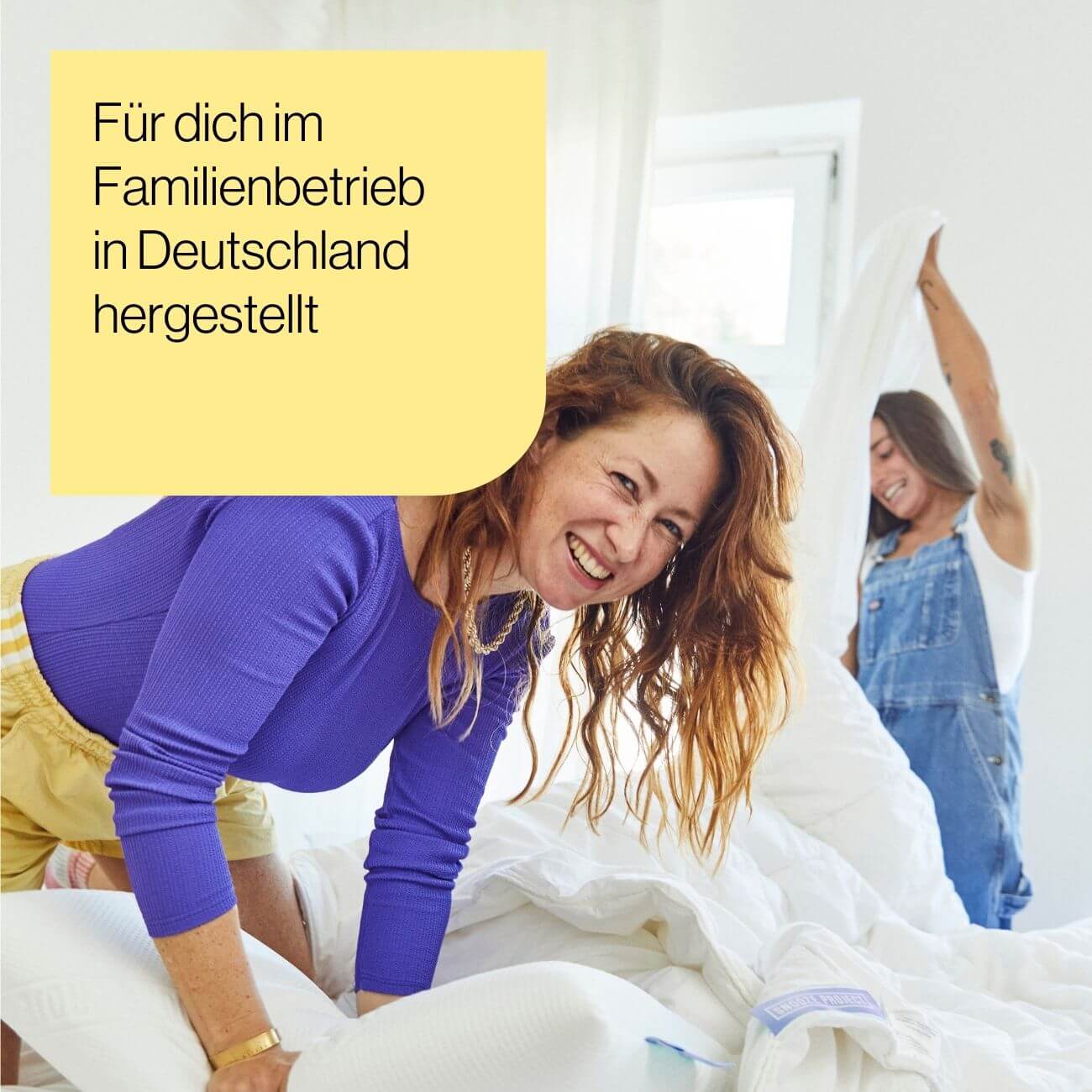 2 Zwei Frauen lächeln und machen zusammen ein Bett in einem hellen Raum. Auf einem gelben Kasten mit deutschem Text steht "Für dich im Familienbetrieb in Deutschland hergestellt".