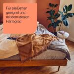 Ein ordentlich gemachtes Holzbett mit grauer und beiger Bettwäsche und einer braunen Überwurfdecke steht neben einem weißen Beistelltisch mit einer Pflanze. Der deutsche Text darüber lautet: Für alle Betten geeignet und mit dem idealen Härtegrad.