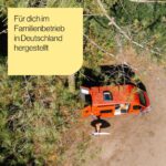Eine Person steht mit einem Surfbrett neben einem orangefarbenen Wohnmobil auf einem Feld, umgeben von grünen Bäumen. Das Arlo Viscoschaum Höhenverstellbare Outdoor-Kissen wird für dich im Familienbetrieb in Deutschland hergestellt.