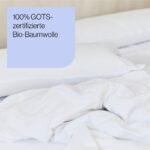 Ein Bett mit weißen, zerknitterten Laken und einem Kopfkissen. In der oberen linken Ecke befindet sich ein blauer Kasten mit deutschem Text: 100% GOTS-zertifizierte Bio-Baumwolle.