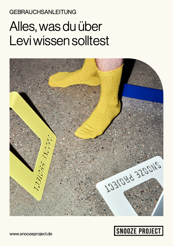 Eine Person in gelben Socken steht auf einem gesprenkelten Boden neben zwei rechteckigen Rahmen, einem gelben und einem weißen, mit der Aufschrift SNOOZE PROJECT. Darüber erscheint ein deutscher Text, darunter Alles, was du über Levi wissen solltest.