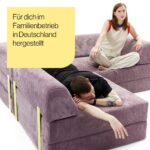 Eine Frau sitzt im Schneidersitz auf einem lilafarbenen Kordsofa, während ein Mann mit dem Gesicht nach unten auf dem Sofa ausgestreckt liegt. Der Text auf Deutsch lautet: Für dich im Familienbetrieb in Deutschland hergestellt.