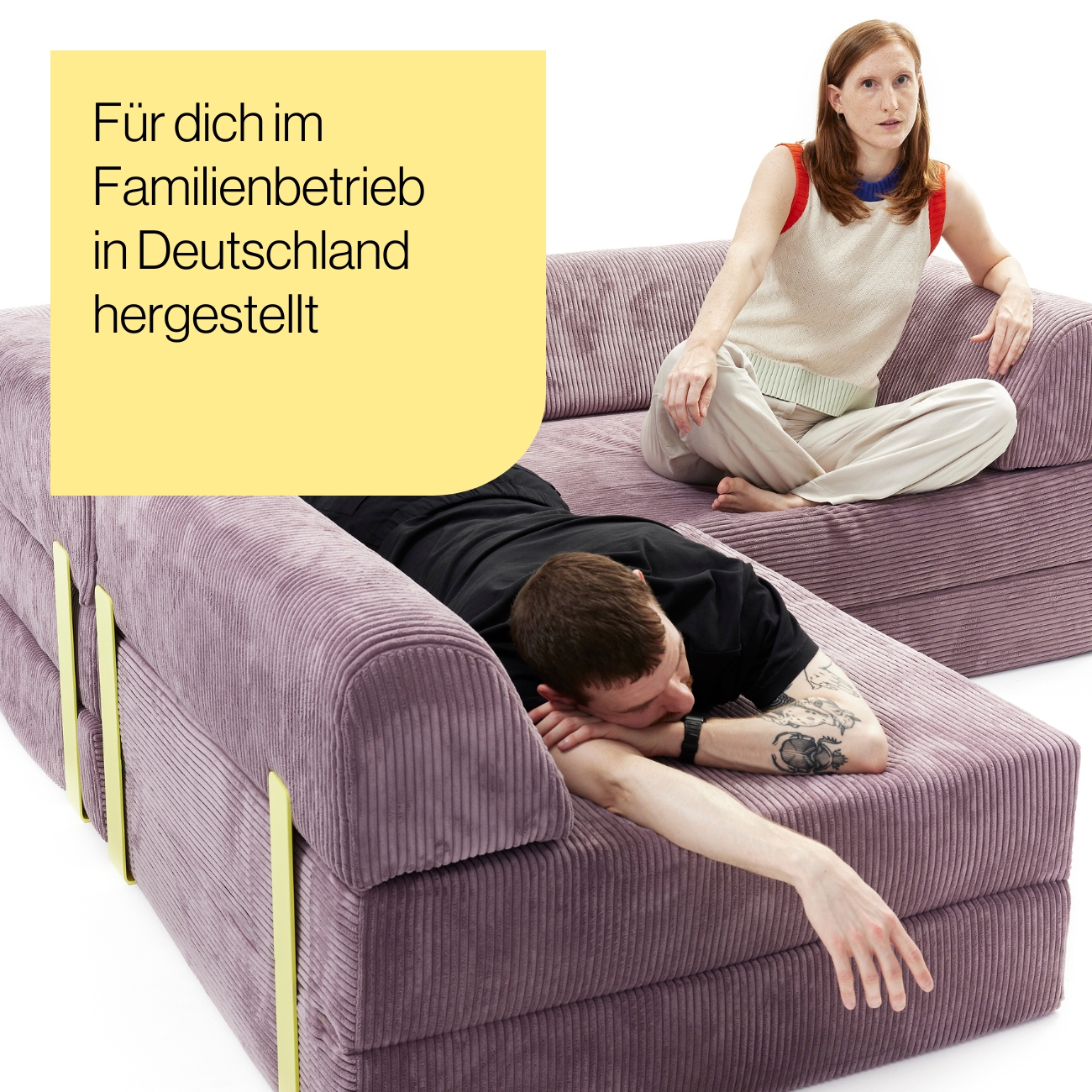 Levi_Produkt-Mood_01a Eine Frau sitzt im Schneidersitz auf einem lilafarbenen Kordsofa, während ein Mann mit dem Gesicht nach unten auf dem Sofa ausgestreckt liegt. Der Text auf Deutsch lautet: Für dich im Familienbetrieb in Deutschland hergestellt.