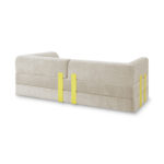 Ein modernes beigefarbenes 2-Sitzer-Sofa mit abgerundeten Kanten und zwei gelben vertikalen Stützbändern entlang der Rückenlehne und der Seiten, abgebildet vor einem weißen Hintergrund.