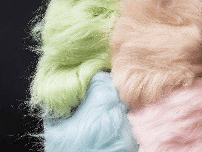 Vier flauschige Strukturstoffe aus Polyacrylfasern in Pastellgrün, Pfirsich, Blau und Rosa sind dicht aneinandergereiht vor einem schwarzen Hintergrund.