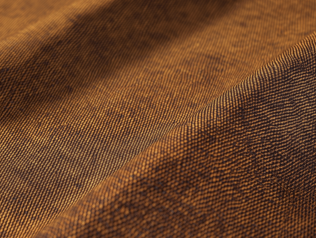 Nahaufnahme eines braunen Mako-Batist-Gewebes mit feinen diagonalen Linien und sichtbarer Bindung, das weiche Falten und eine sanft gewellte Oberfläche aufweist.