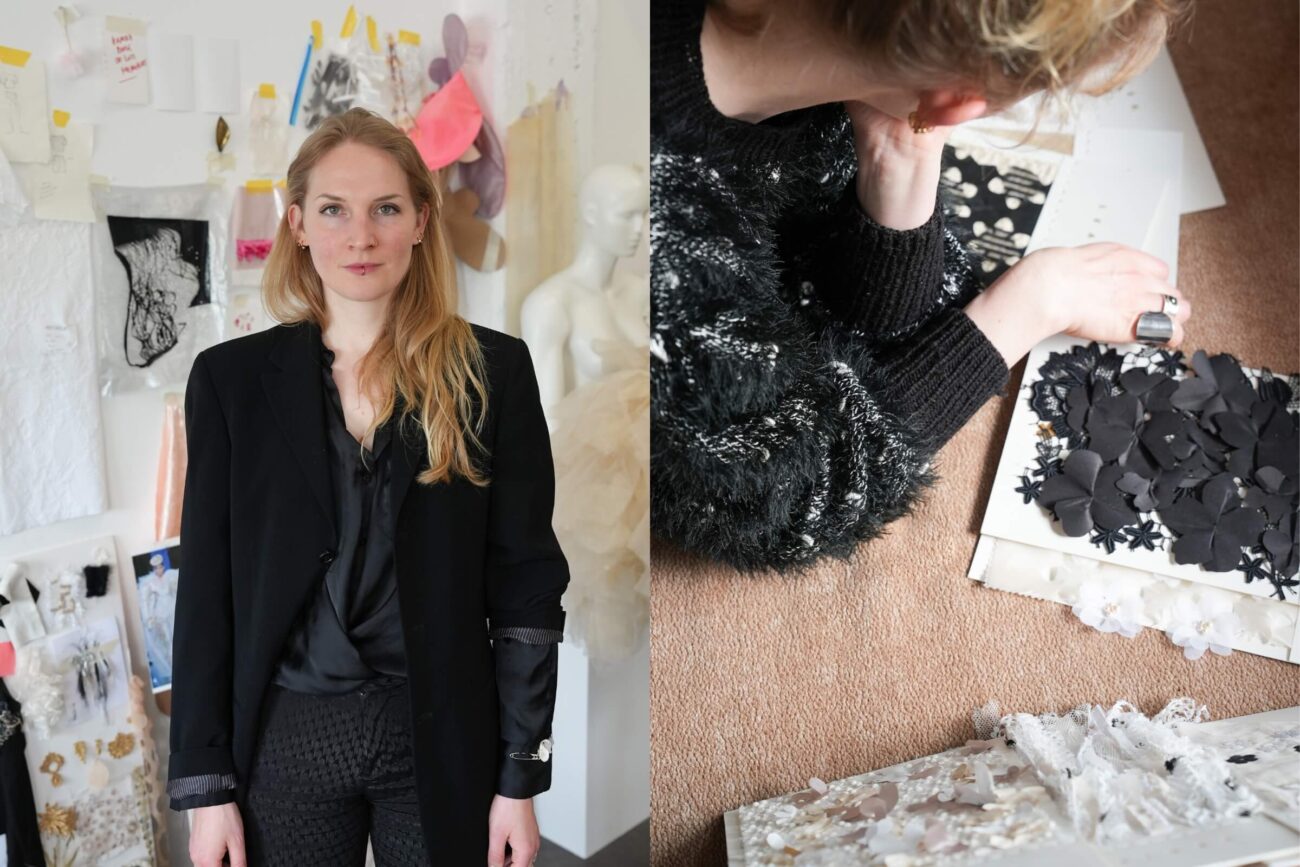 Eine Frau mit langen blonden Haaren steht in einem Atelier mit Designskizzen und Stoffmustern an der Wand. Neben ihr sind in einer Nahaufnahme Hände zu sehen, die auf einem Tisch ein Muster aus schwarzem, geblümtem Stoff mit Struktur bearbeiten.