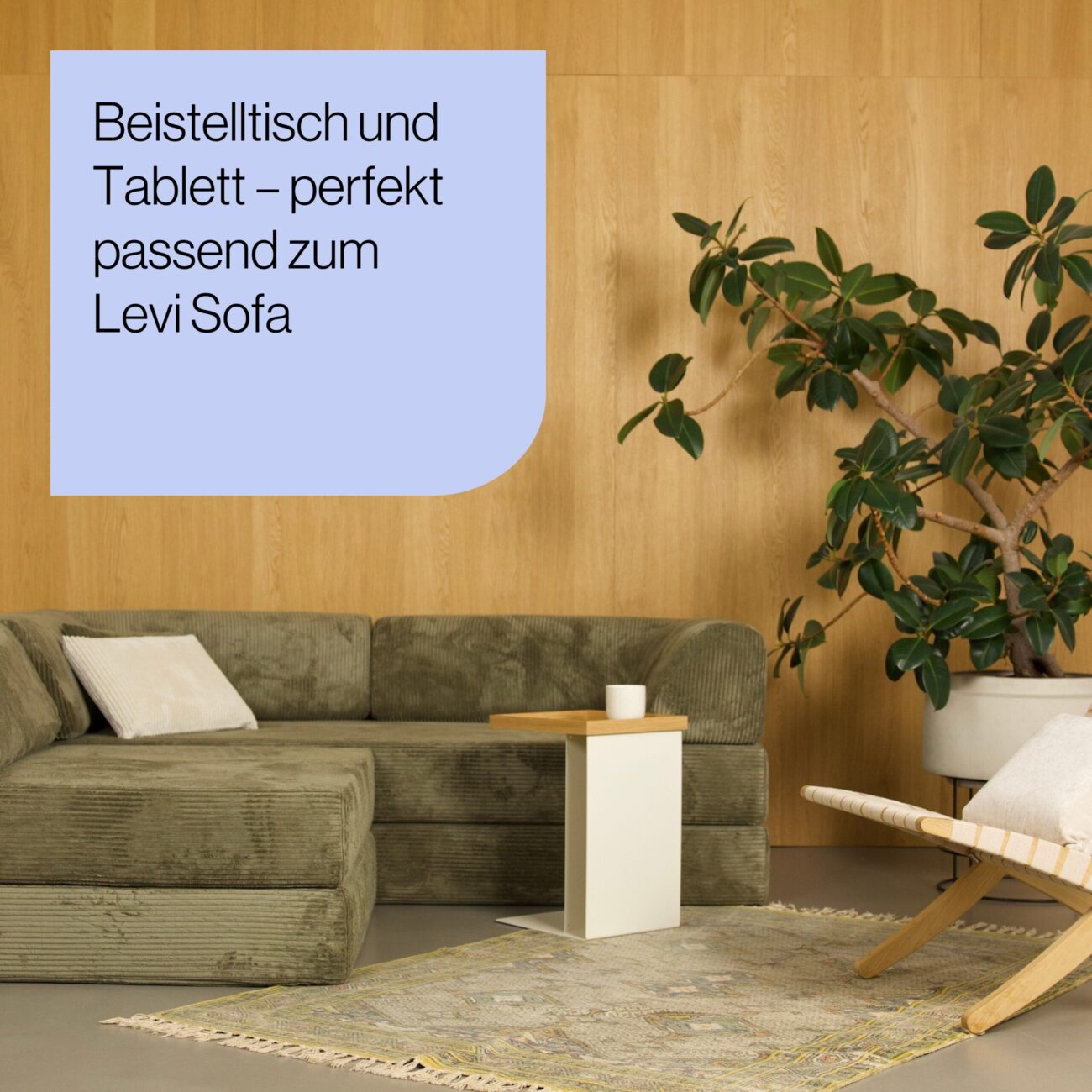 Tade_Produkt Mood_02 Ein modernes Wohnzimmer mit einem grünen Sektionssofa, einem kleinen weißen Beistelltisch mit einem Holztablett, einem gemusterten Teppich, einem Sessel, einer großen Topfpflanze und einer holzgetäfelten Wand. Der deutsche Text ist in einem blauen Kasten eingeblendet.