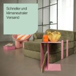 Ein modernes Wohnzimmer mit einem grünen Sofa, einem rosa Beistelltisch mit einer orangefarbenen Tasse und einer gelben Vase sowie einem rosa Stuhl im Hintergrund. Der Text lautet: Schneller und klimaneutraler Versand.
