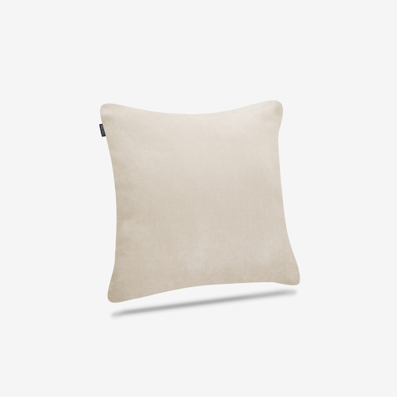 SPKOTTI80x80-SC-TW-img001 Ein quadratisches, hellbeiges Kissen mit weicher Textur wird vor einem schlichten weißen Hintergrund gezeigt. An der oberen linken Seite ist ein kleines schwarzes Etikett angebracht. Das Kissen scheint über einem schwachen Schatten zu schweben.