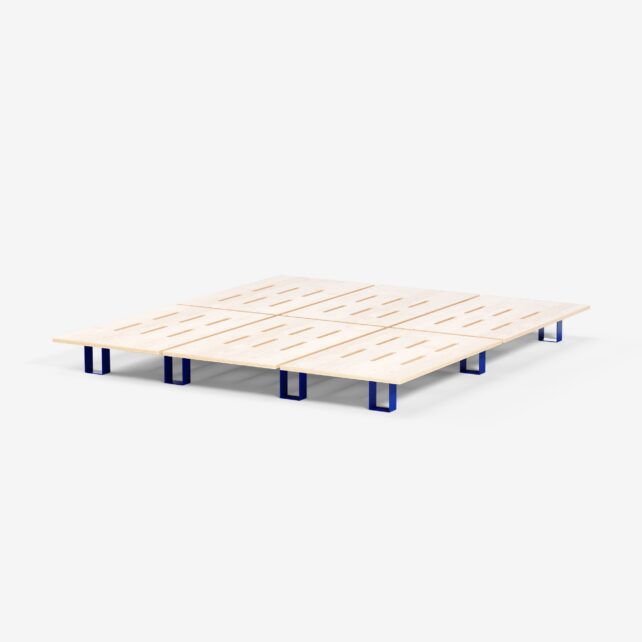 Ein minimalistisches Bettgestell aus hellem Holz mit horizontalen Latten und kurzen, blauen, rechteckigen Beinen, das auf einem schlichten weißen Hintergrund abgebildet ist.