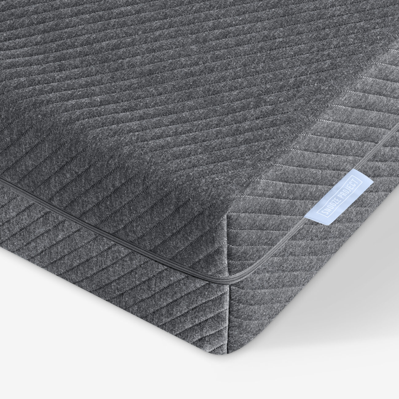 Nahaufnahme der Ecke einer grauen Matratze mit einer strukturierten, gesteppten Oberfläche und einem hellblauen Etikett. Die Nähte und das Stoffmuster sind deutlich zu erkennen.