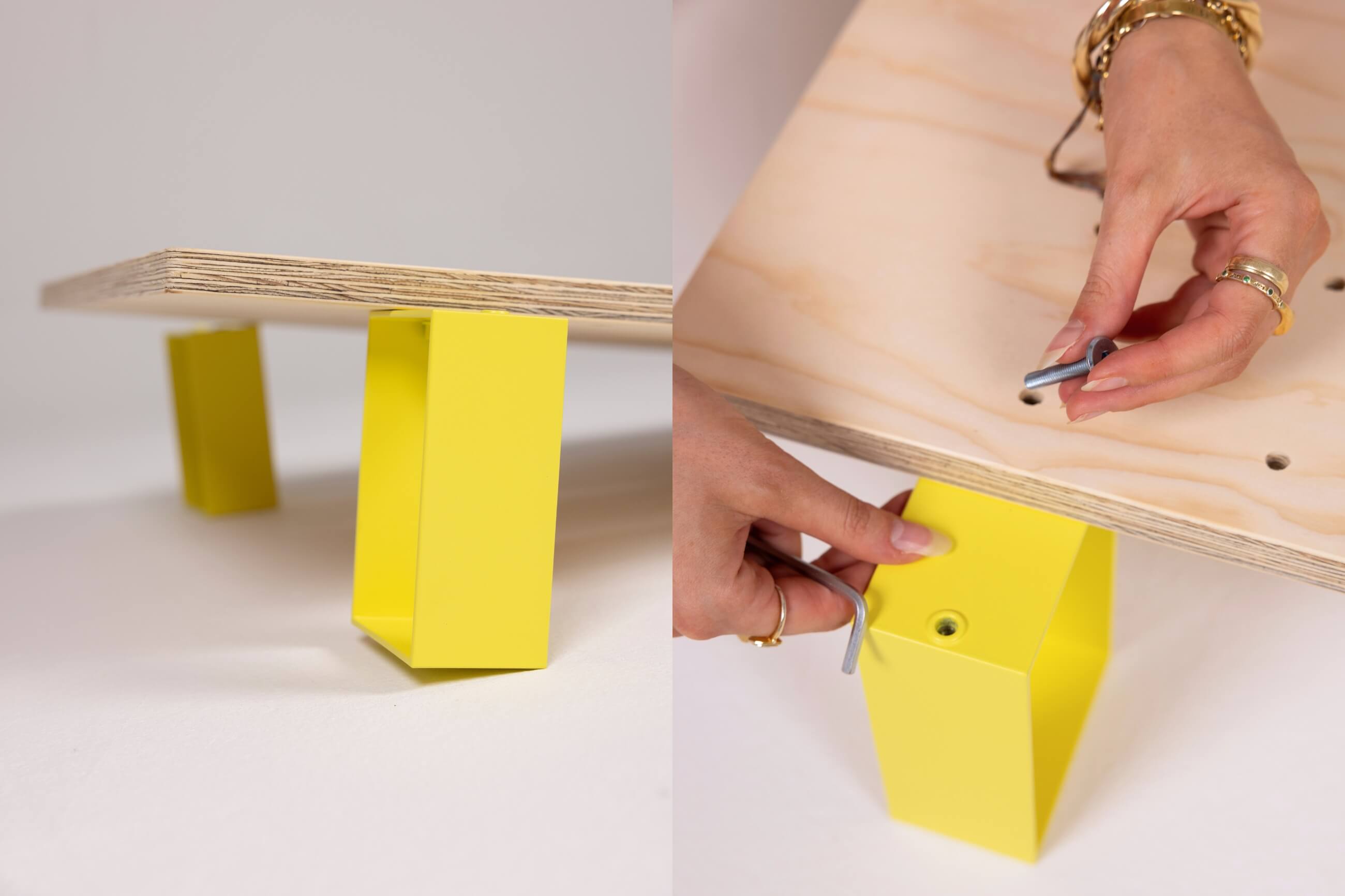 Nahaufnahme eines Holzbretts mit leuchtend gelben Metallbeinen; die Hände einer Person befestigen ein gelbes Bein mit Schrauben und einem Inbusschlüssel an dem Brett.
