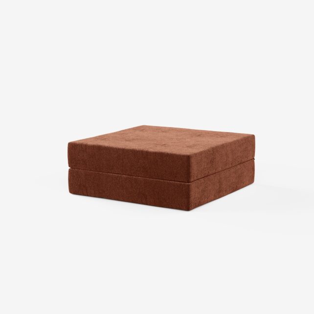 Ein quadratischer, brauner, stoffbezogener Ottoman mit weicher, plüschiger Textur vor einem schlichten weißen Hintergrund.