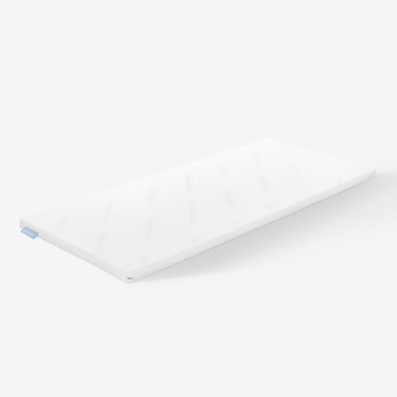 SPTFAM_img002 Eine dünne, rechteckige, weiße Matratzenauflage mit einem dezenten Strukturmuster und einem kleinen blauen Anhänger an einer Ecke auf einem schlichten weißen Hintergrund.