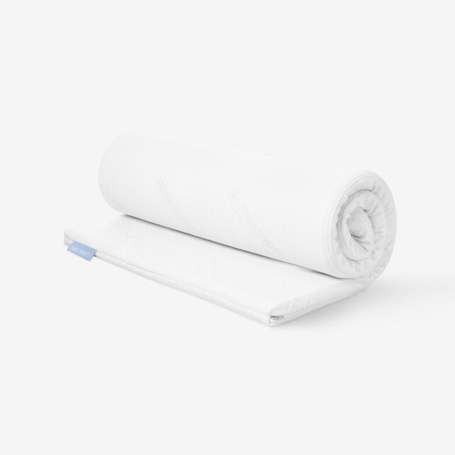 Eine aufgerollte weiße Matratzenauflage wird teilweise auf einem weißen Hintergrund ausgerollt und zeigt ihre glatte, gesteppte Oberfläche und ihr klares, minimalistisches Design.