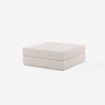 Ein moderner, minimalistischer, hellbeiger, quadratischer Hocker mit subtilen horizontalen, strukturierten Linien vor einem schlichten weißen Hintergrund.