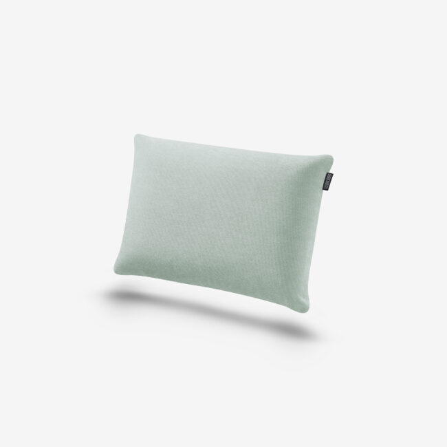 Ein hellgrünes, rechteckiges Kissen mit glatter Oberfläche und einem kleinen schwarzen Schildchen auf einer Seite, das vor einem schlichten weißen Hintergrund steht.