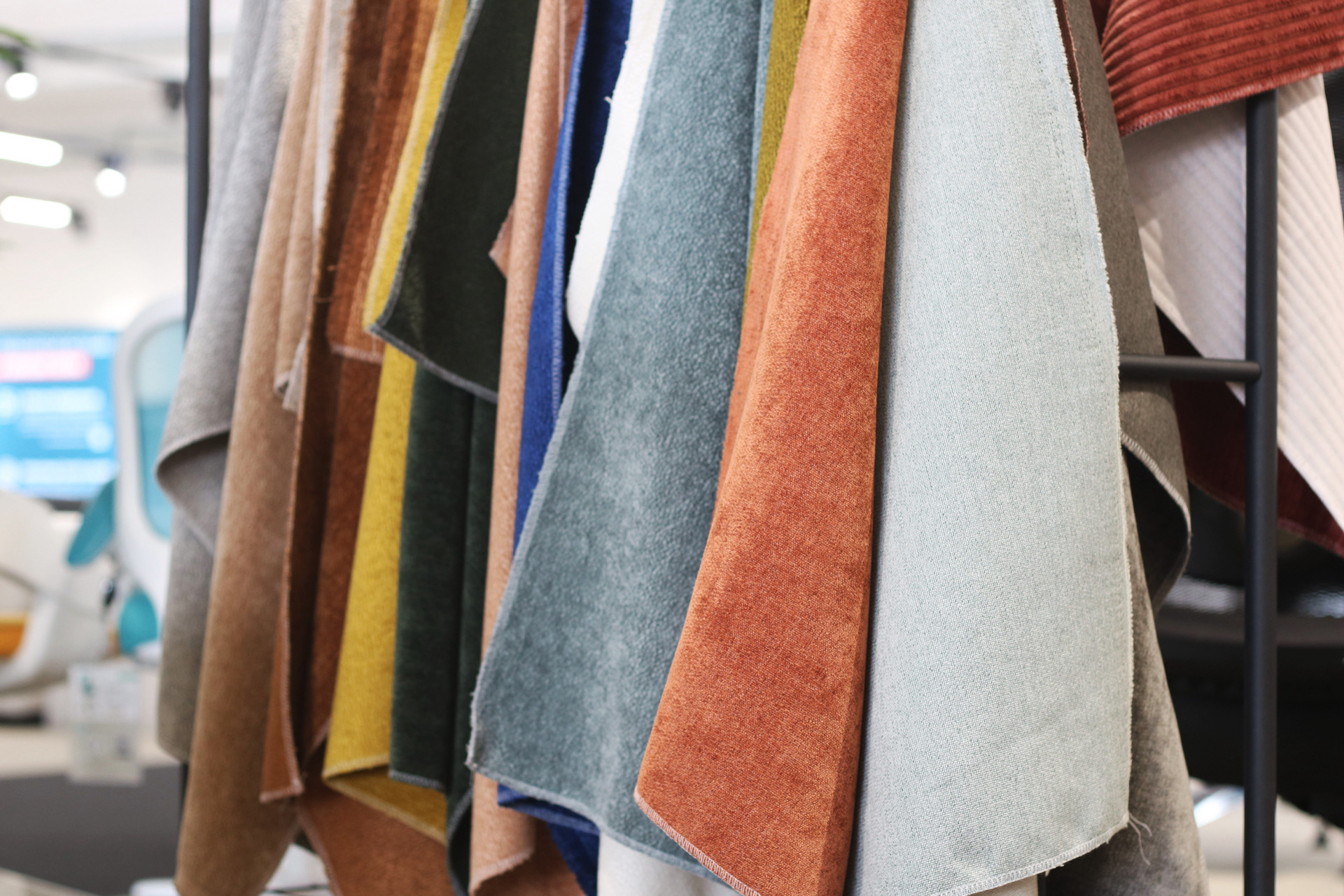 Nahaufnahme von verschiedenfarbigen Stoffmustern, die in einem gut beleuchteten Ausstellungsraum des Snooze-Projekts vertikal aufgehängt sind, mit Schattierungen von Braun, Gelb, Blau, Orange, Grün und Grau.
