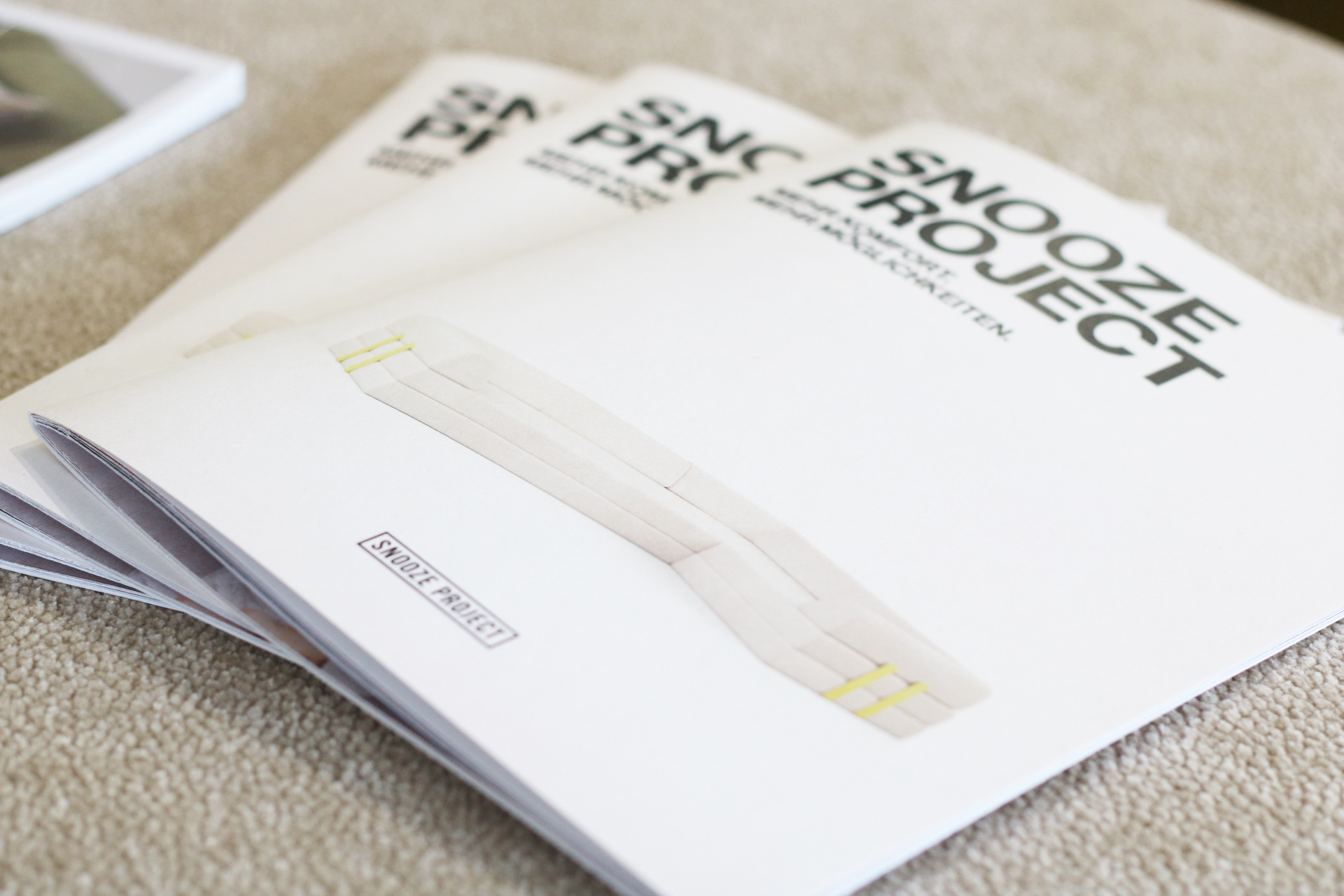 Drei Broschüren mit dem Titel Snooze Project sind auf einer strukturierten beigen Oberfläche gestapelt, jede mit einer minimalistischen Sofa-Illustration auf dem Cover - perfekt für Freunde von Snooze Project oder diejenigen, die unsere Ausstellungsräume erkunden.