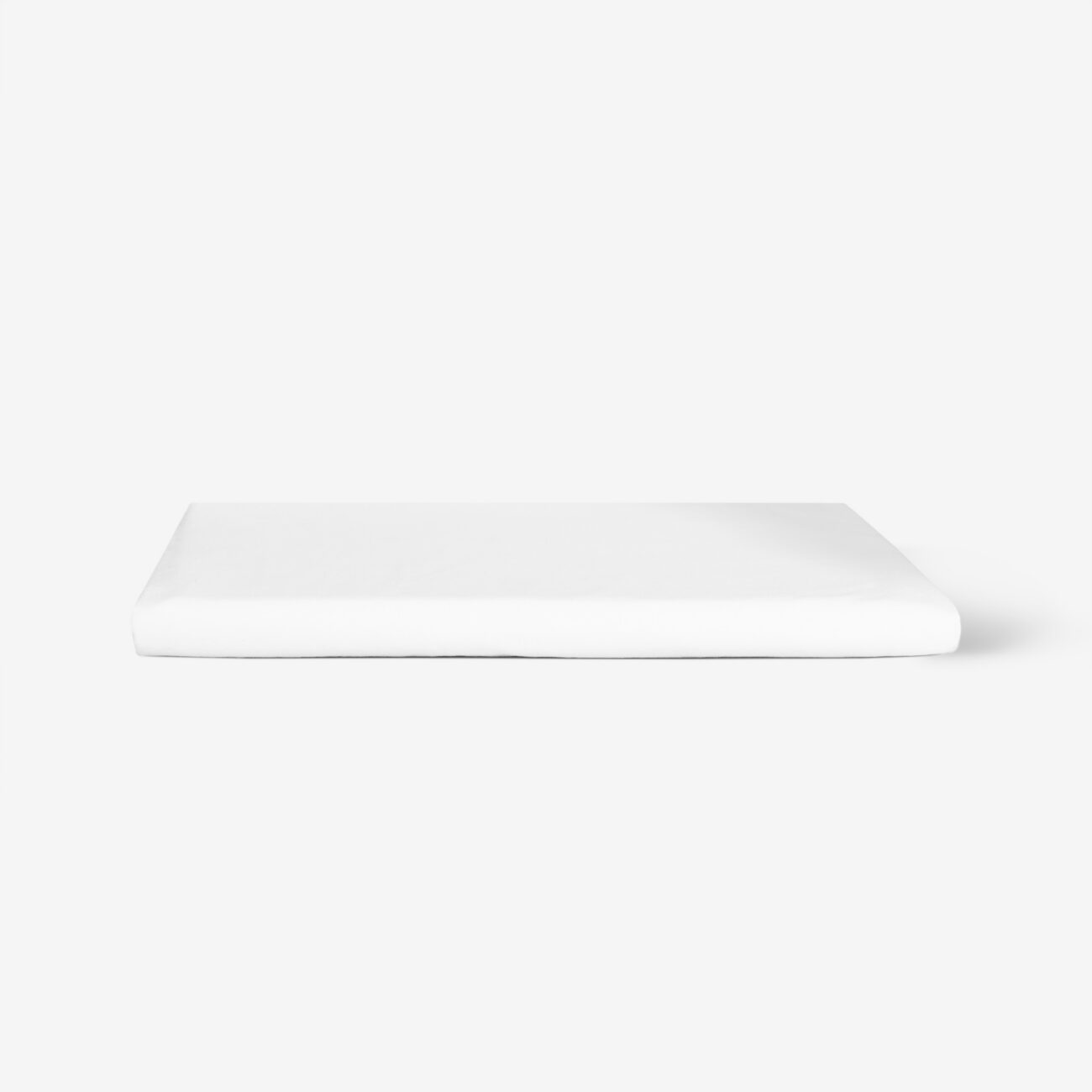 Ein fein säuberlich gefaltetes weißes Bettlaken liegt auf einer schlichten weißen Fläche mit minimalistischem Hintergrund.