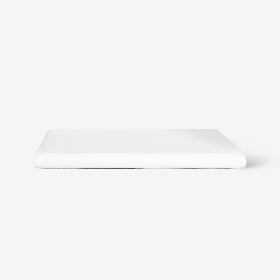 Ein fein säuberlich gefaltetes weißes Bettlaken liegt auf einer schlichten weißen Fläche mit minimalistischem Hintergrund.