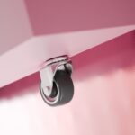 Nahaufnahme eines einzelnen Lenkrollens, das an der Unterseite einer rosa, strukturierten Metalloberfläche befestigt ist, mit sanfter Beleuchtung und unscharfem Hintergrund.